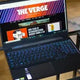 Lenovo Ideapad laptop with backlit keyboard on glass table, Verge website on screen
