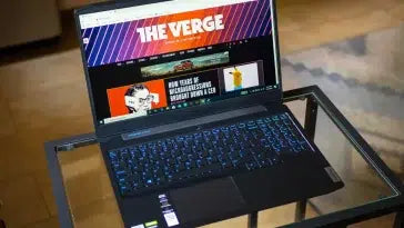 Lenovo Ideapad laptop with backlit keyboard on glass table, Verge website on screen
