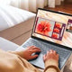 Person using a slim laptop on a sofa, vibrant display showing flower images, natural light